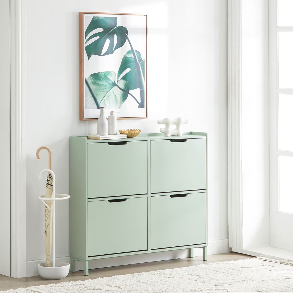 A mint green shoe cabinet with four flip-down drawers stands against a white wall, next to a white umbrella stand. A framed botanical print hangs above the cabinet.