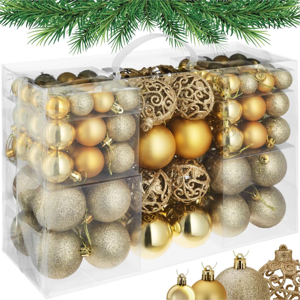 A clear, well-lit studio shot of a set of gold and silver Christmas ornaments in a clear plastic box, with a sprig of green pine needles across the top.