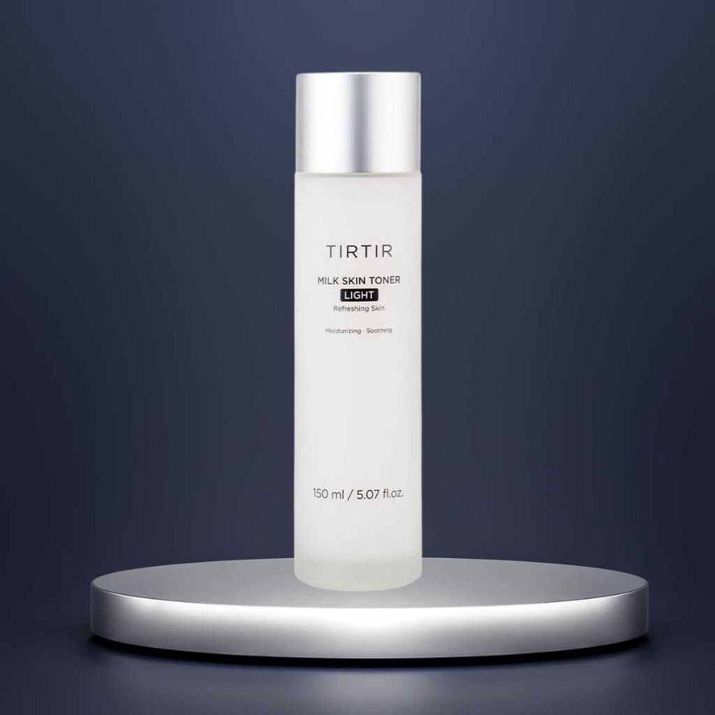 A bottle of Tirtir Milk Skin Toner Light is displayed on a silver pedestal against a dark blue background.