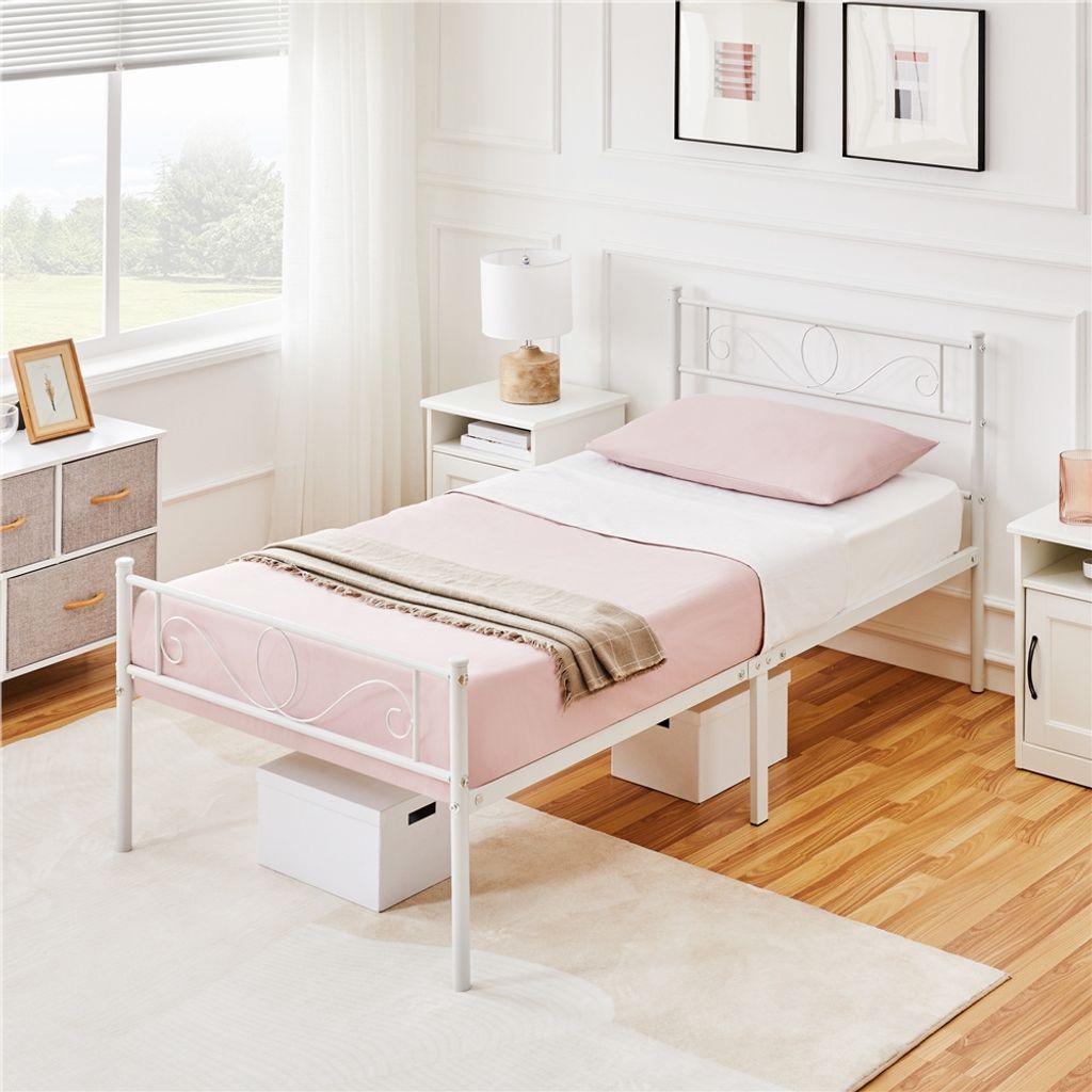 A bedroom scene with a white metal bed frame, pink bedding, and a bedside table.