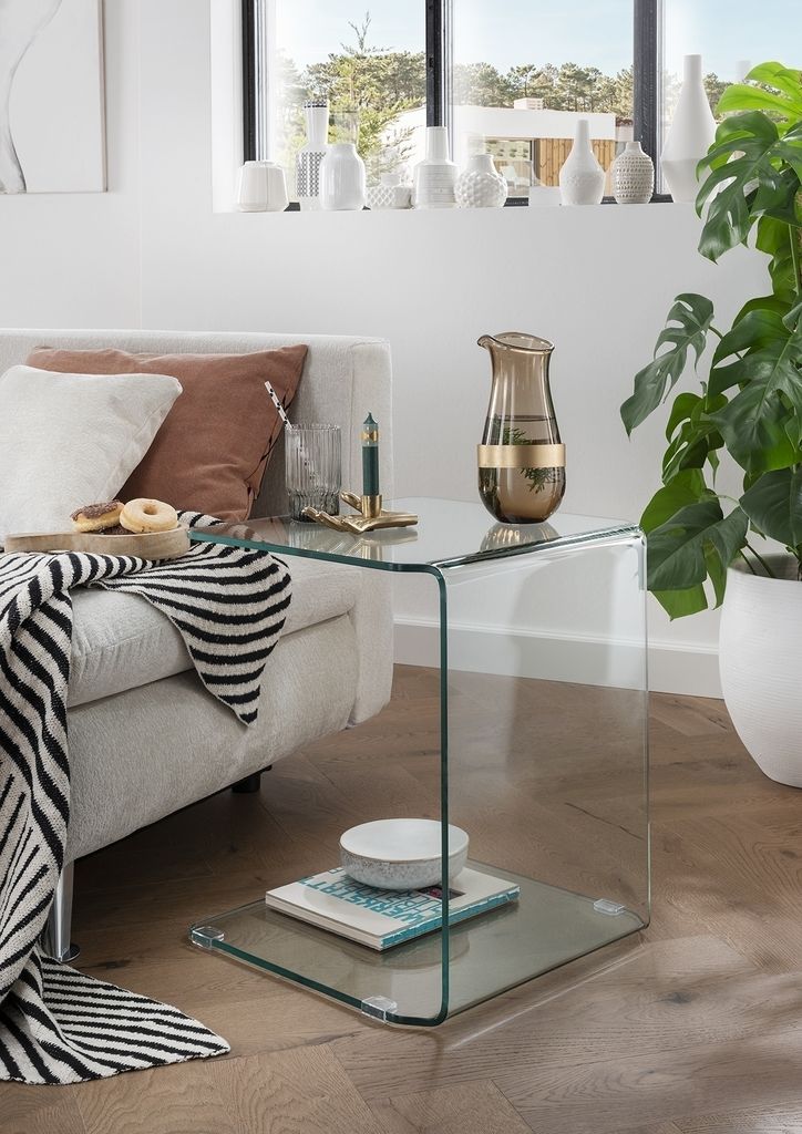 A glass side table next to a sofa, with a vase and books on it.