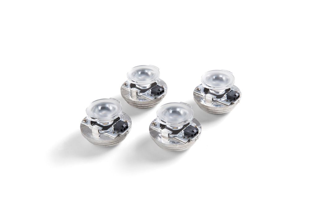 Four small, metallic-looking objects with clear plastic tops, arranged diagonally on a white background.
