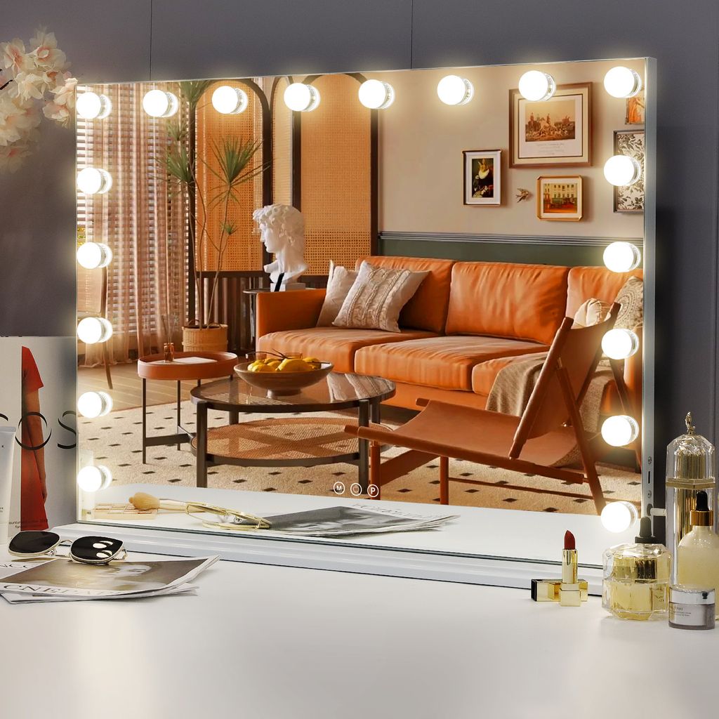 A vanity mirror with lights reflecting a living room scene, placed on a white surface with makeup items.