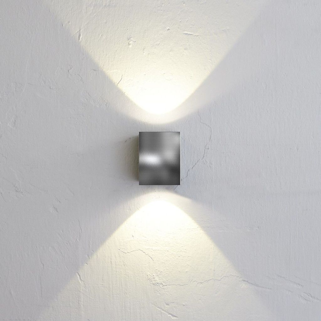 A square, metallic wall light fixture mounted on a textured white wall, casting light upwards and downwards.