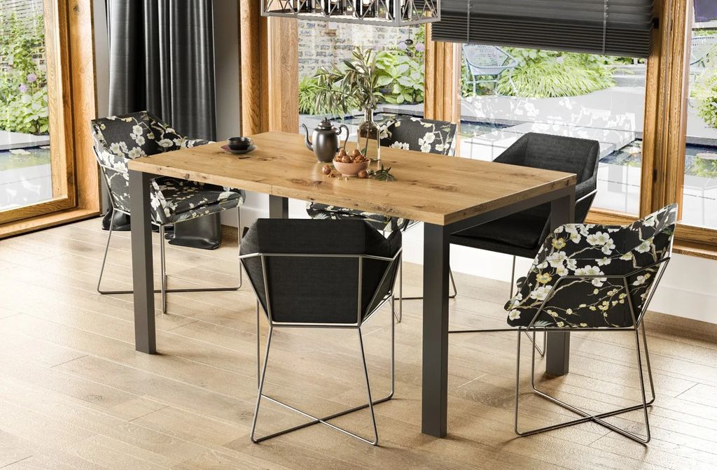 A dining table and chairs set in a well-lit room with large windows overlooking a garden and water feature.
