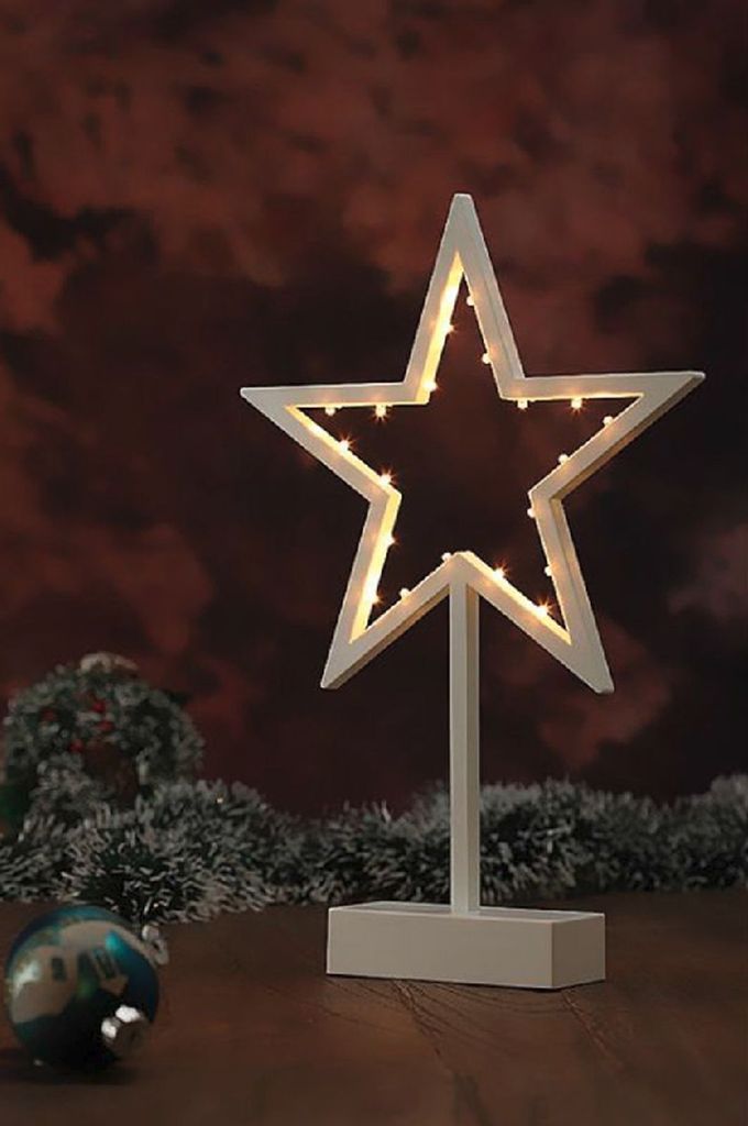 A decorative LED star with lights on a stand, placed on a wooden surface with festive decorations in the background.