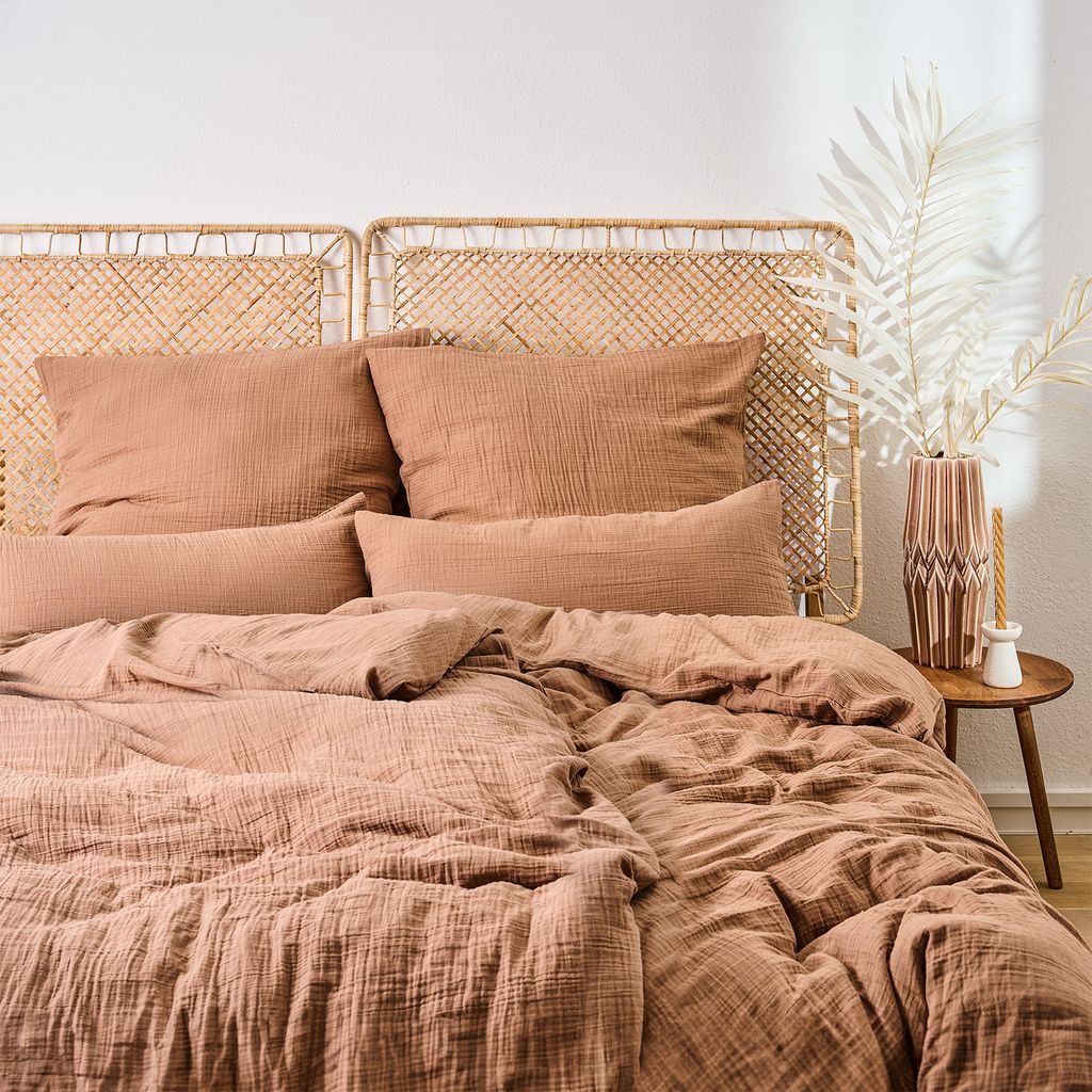A neatly made bed with a woven headboard and textured bedding in a warm, earthy tone.