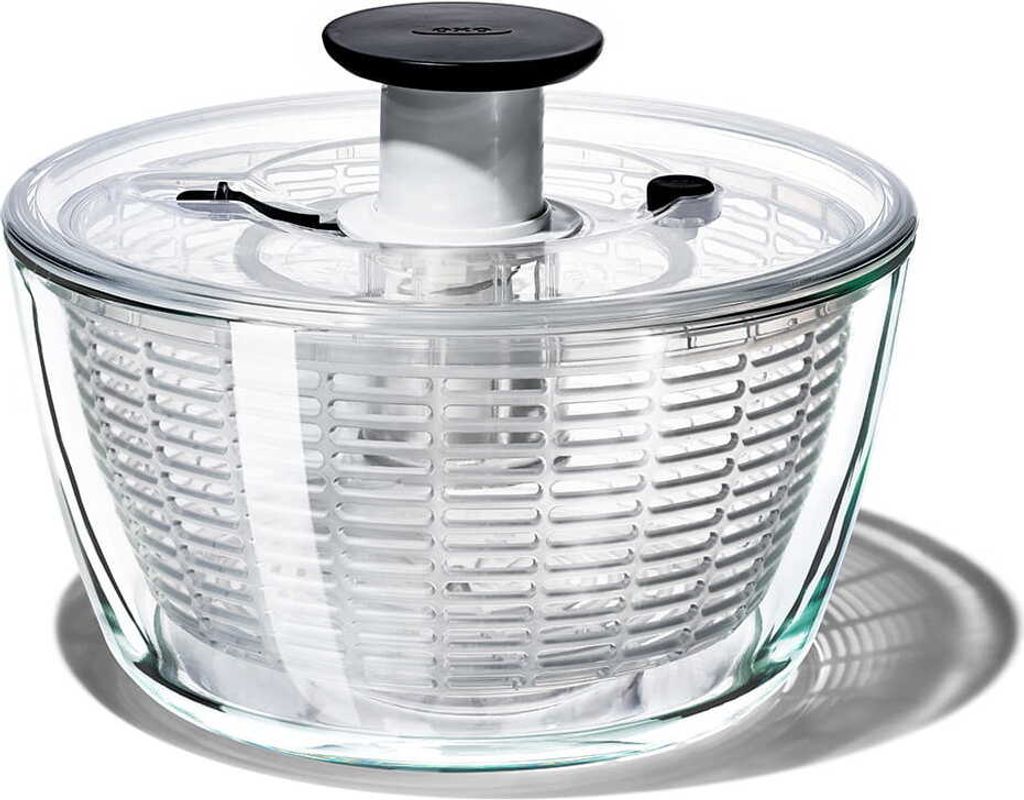 A glass salad spinner with a clear lid and a black and white mechanism on a white background.