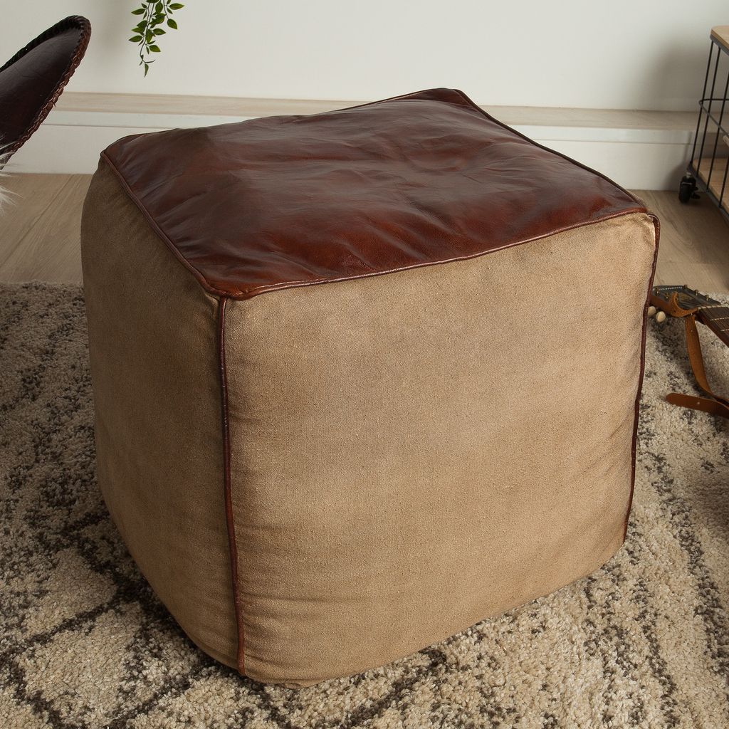 A close-up view of a cube-shaped ottoman with a brown leather top and beige fabric sides, placed on a rug.