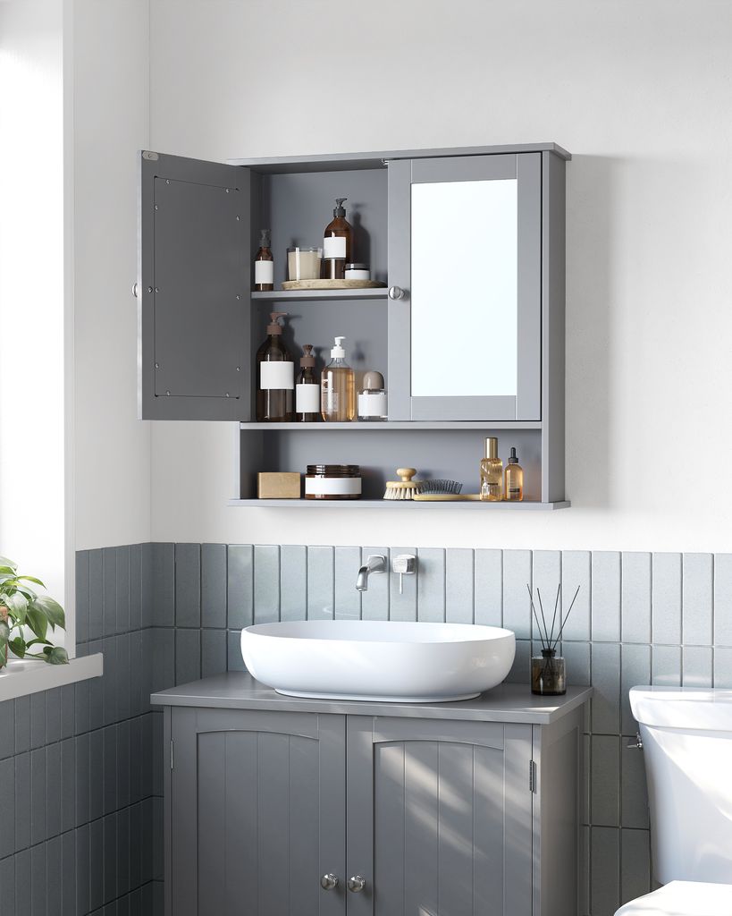 A gray bathroom cabinet with a mirror and open doors, displaying various toiletries. Below the cabinet is a white sink on a gray vanity. The wall is tiled with light blue vertical tiles.