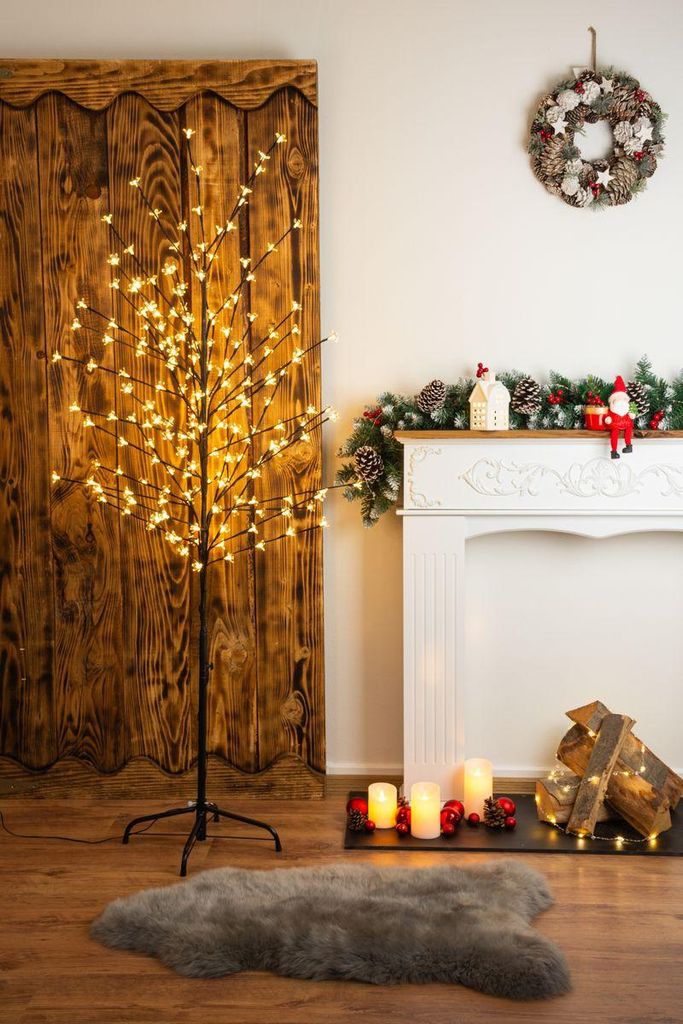 A lit-up decorative tree with warm white lights stands next to a fireplace decorated for Christmas.