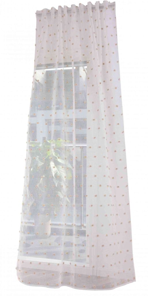 A sheer curtain with pompom details hanging in front of a window.