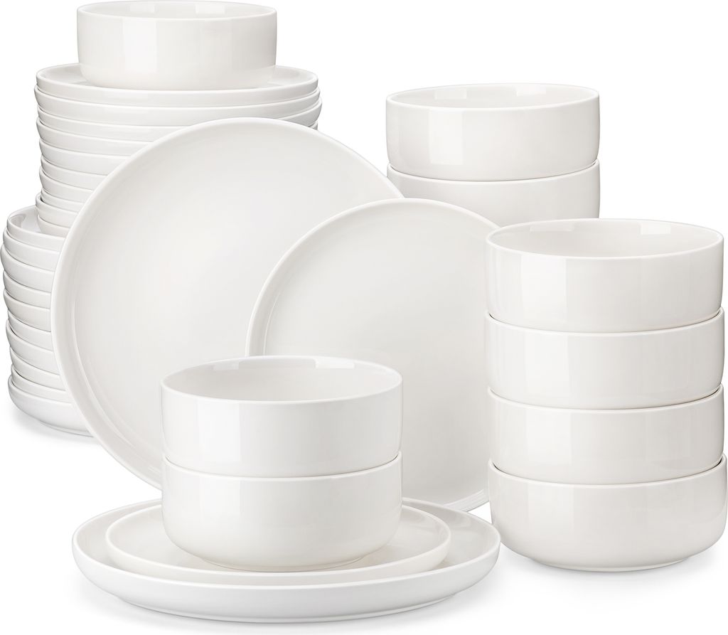 A collection of white ceramic plates and bowls are stacked and arranged on a white background.
