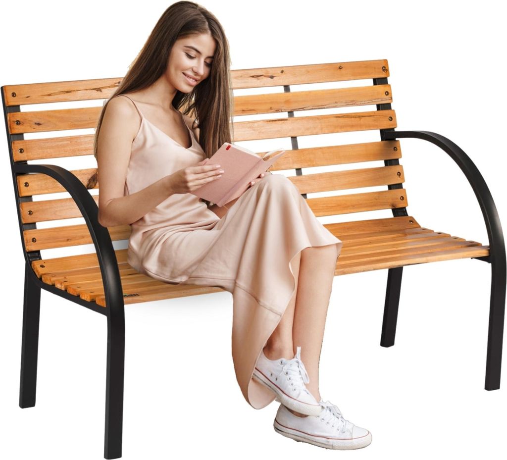 A woman is sitting on a wooden park bench and reading a book.