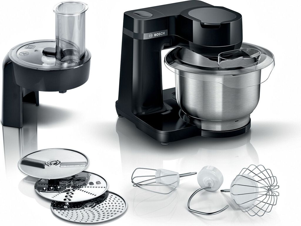 A black Bosch kitchen machine with a stainless steel bowl and various attachments, including a food processor and different beaters, is displayed on a white reflective surface.