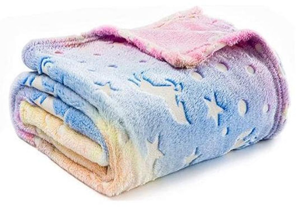 Zusammengefaltete mehrfarbige Decke mit pastellfarbenem Regenbogenverlauf und geprägten, im Dunkeln leuchtenden Einhörnern und Sternen