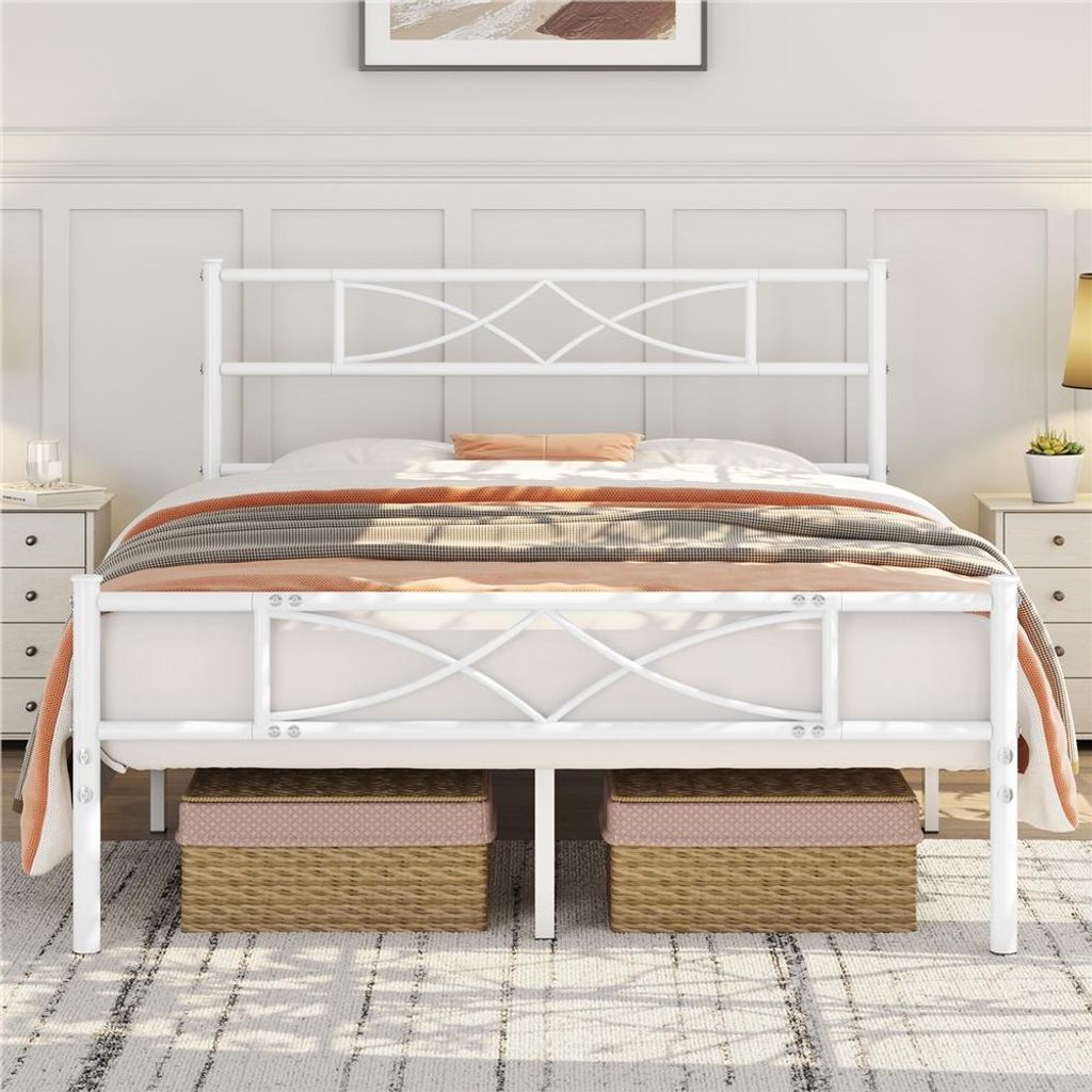 A white metal bed frame with a decorative headboard and footboard, dressed with bedding and blankets. Two storage baskets are placed underneath the bed.