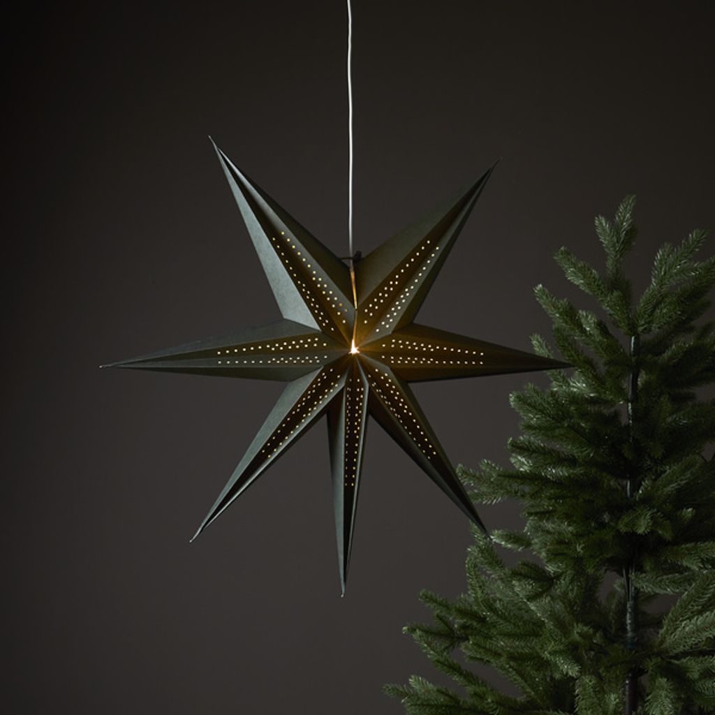 A dark green, seven-pointed star-shaped lantern hangs in front of a dark gray background, with a portion of a green Christmas tree visible on the right.