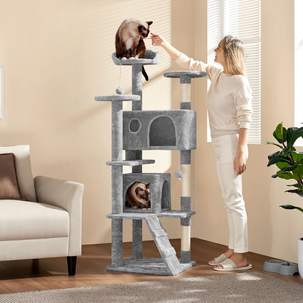 A woman is interacting with a cat on a tall cat tree in a living room.