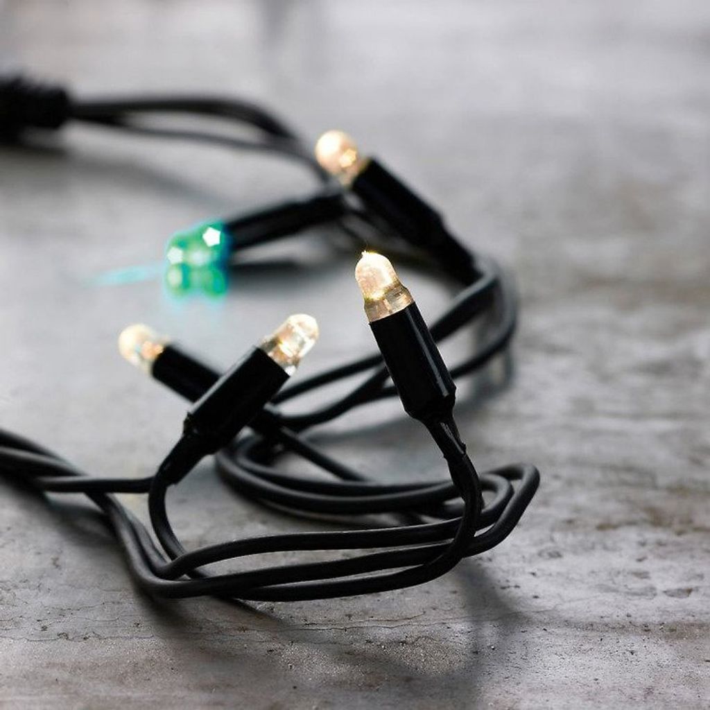 A close-up shot of a string of LED lights with black wires and white and green bulbs, resting on a textured gray surface.