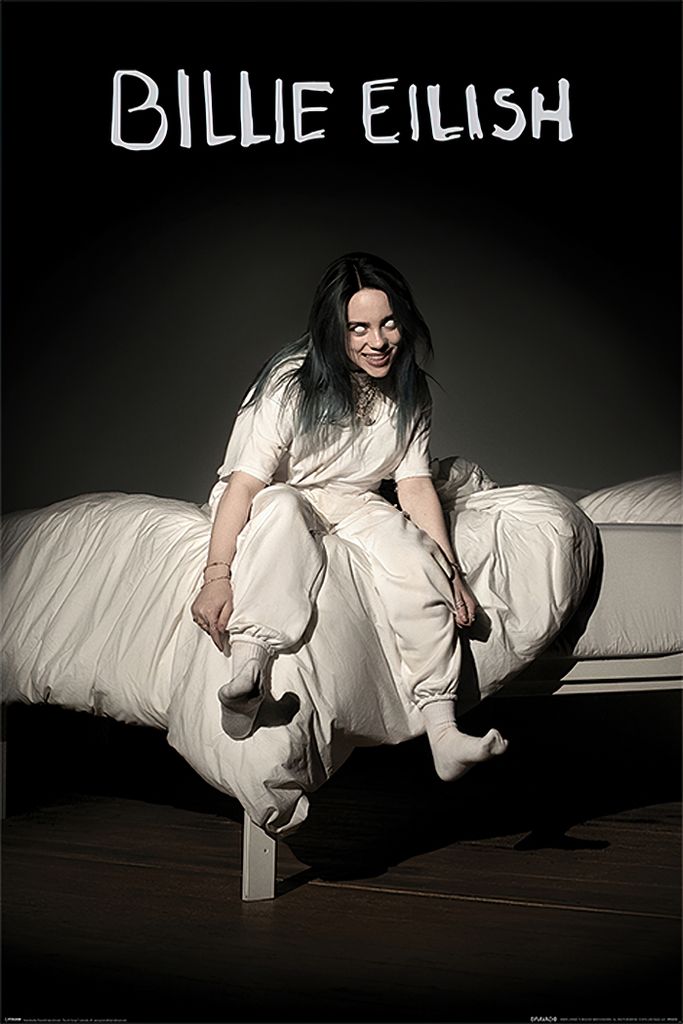 Billie Eilish sitting on a bed with white sheets.