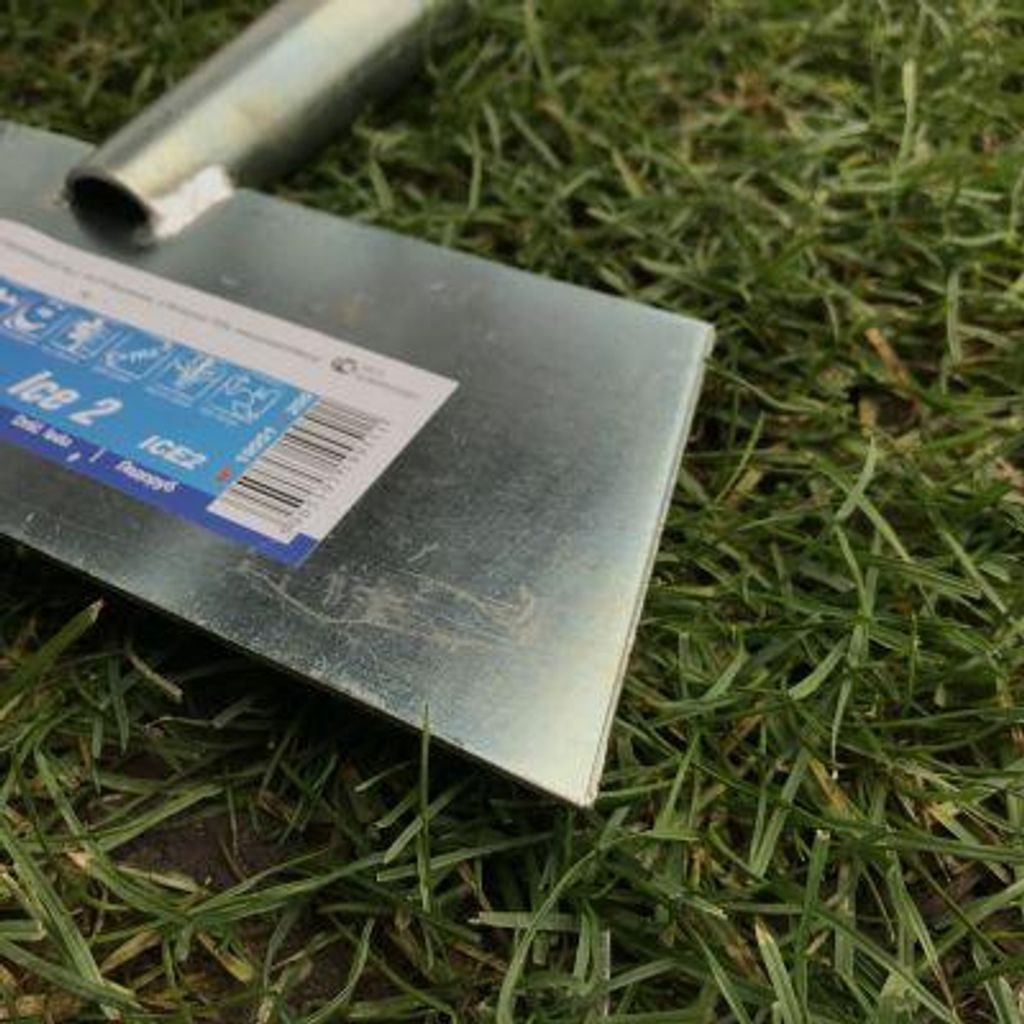 A close-up of a metal trowel lying on grass.