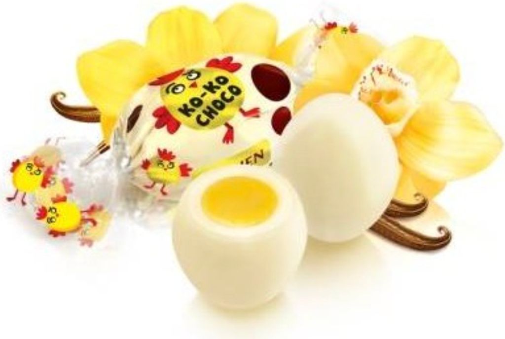 A close-up of white chocolate candies shaped like eggs, with yellow filling, surrounded by yellow orchid petals and vanilla beans.