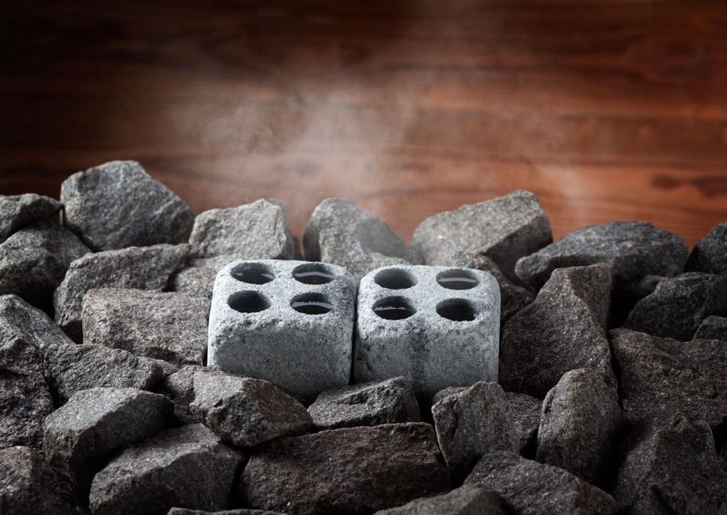 Two stone cubes with four holes each, surrounded by sauna stones, with steam rising in the background.