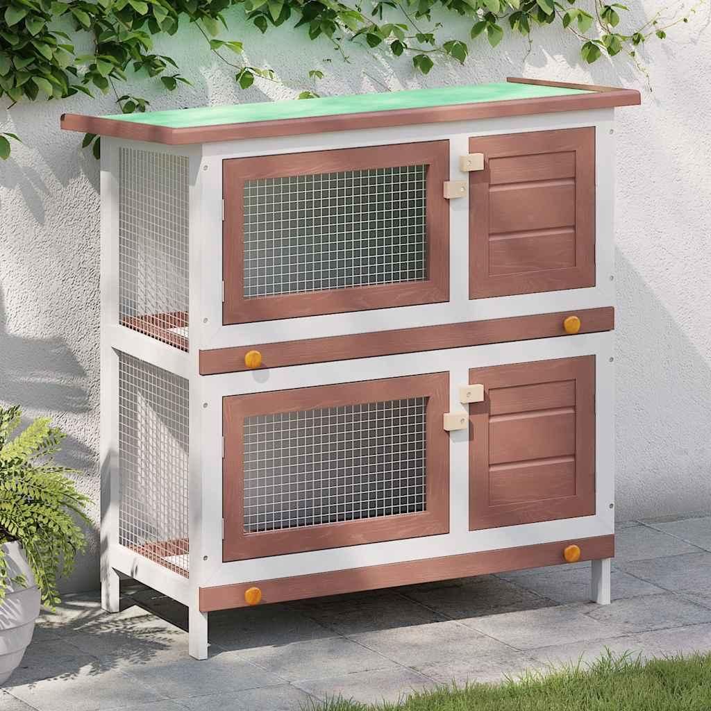 A two-tiered wooden rabbit hutch with a green roof, placed outdoors on a paved patio with grass and a wall with ivy in the background.
