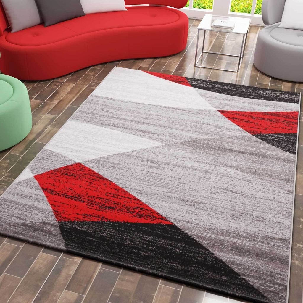 A modern living room with a red sofa, a geometric rug, and a green ottoman.