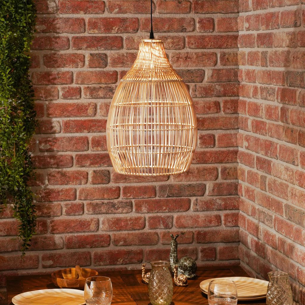 A hanging lamp made of rattan is shown above a dining table with brick walls in the background.