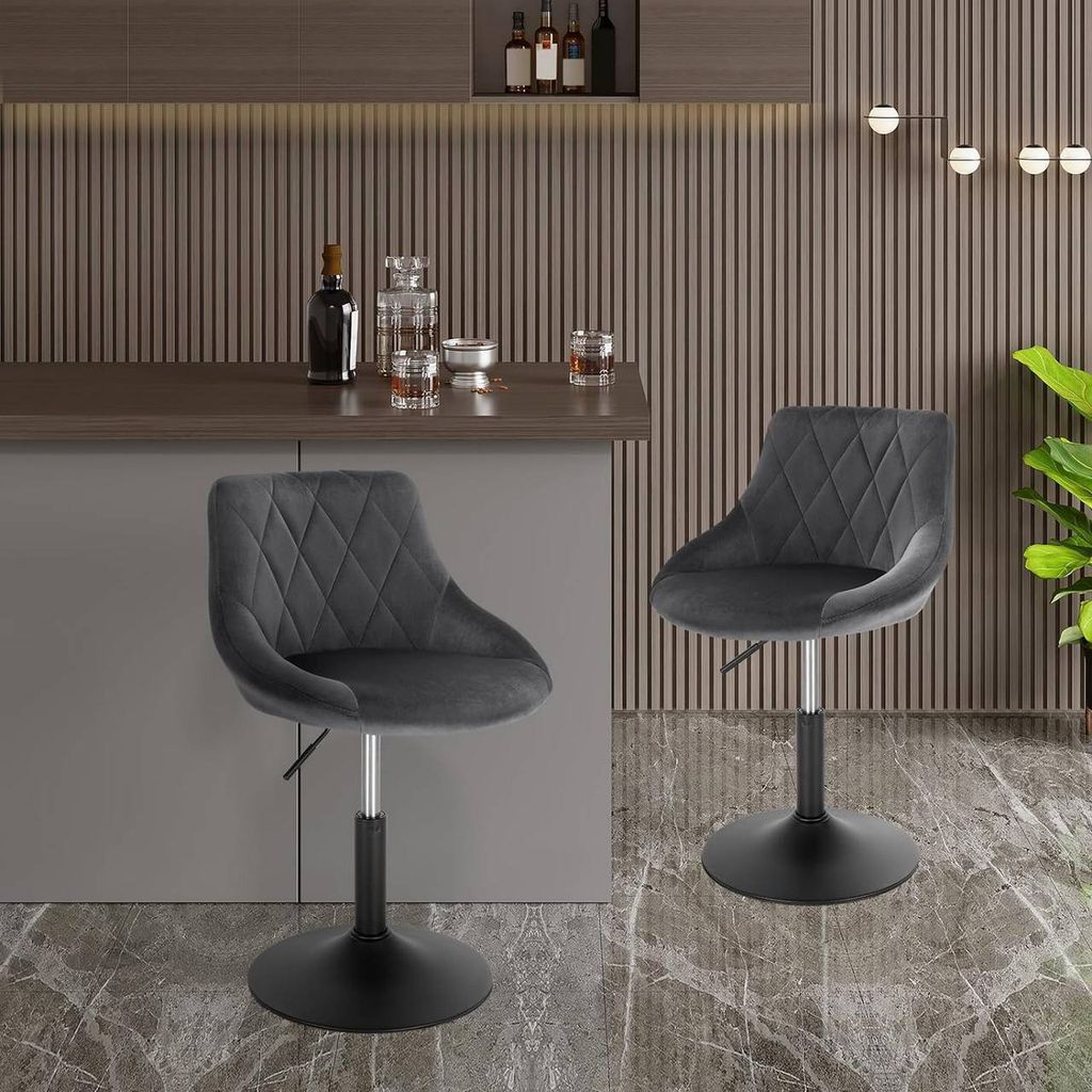 Two dark gray velvet bar stools are shown in a modern kitchen or bar area, with a counter and bottles on it in the background.