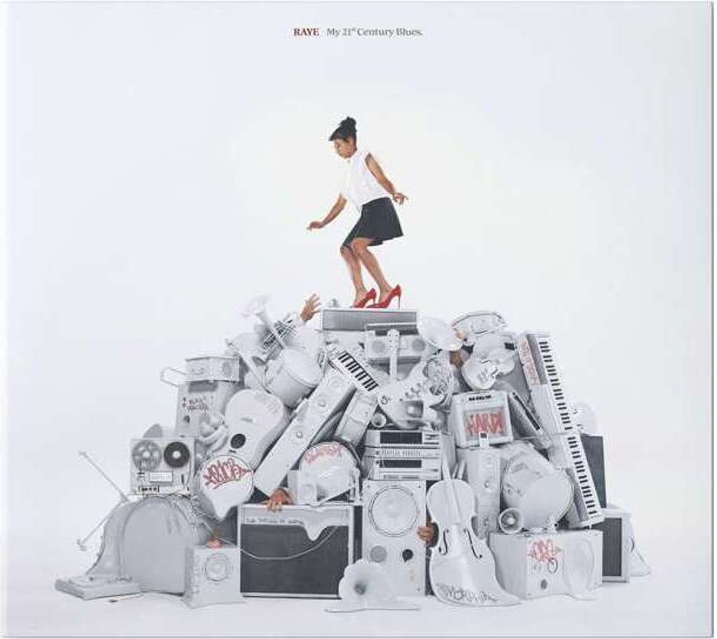 A woman stands on a pile of musical instruments and audio equipment.