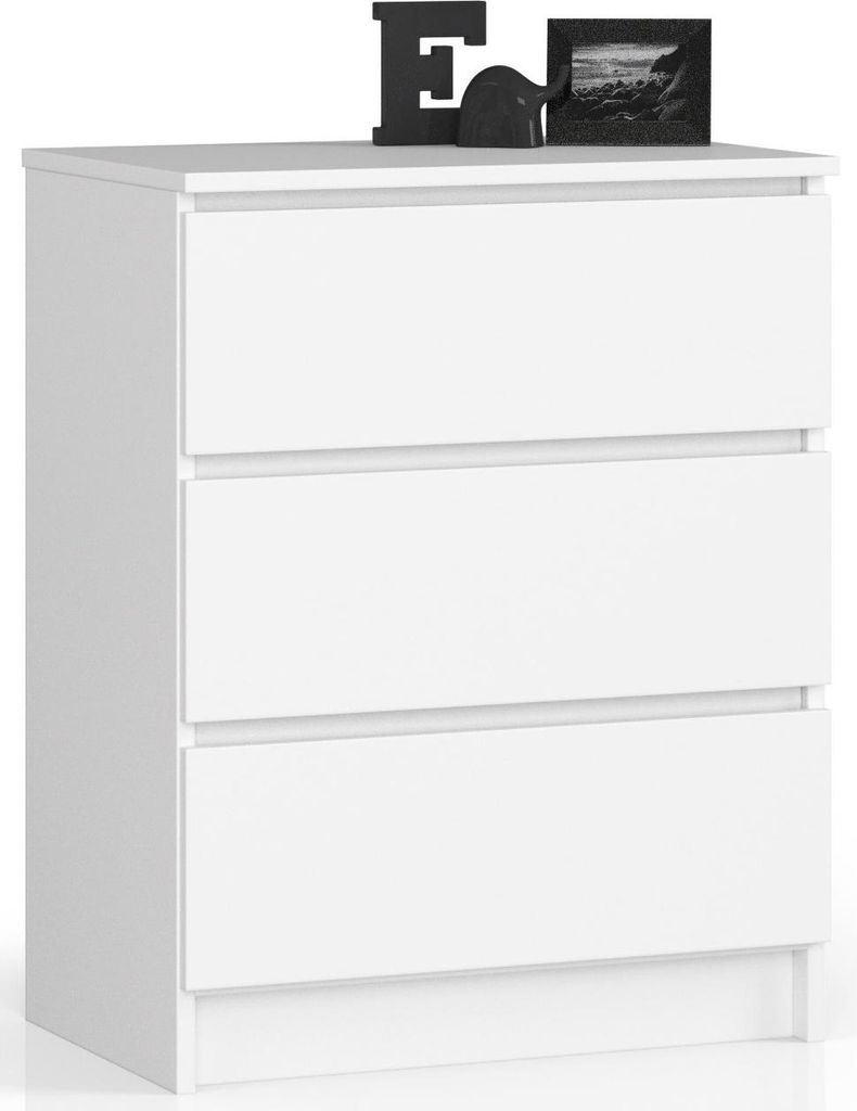 A white chest of drawers with three drawers, shown from the front-left angle. Decorative items, a letter 'E' and a framed picture, are placed on top of the dresser.