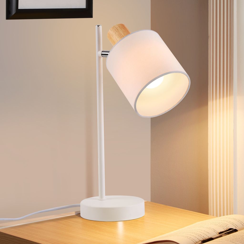 A white desk lamp with a fabric shade and wooden accent sits on a wooden desk.
