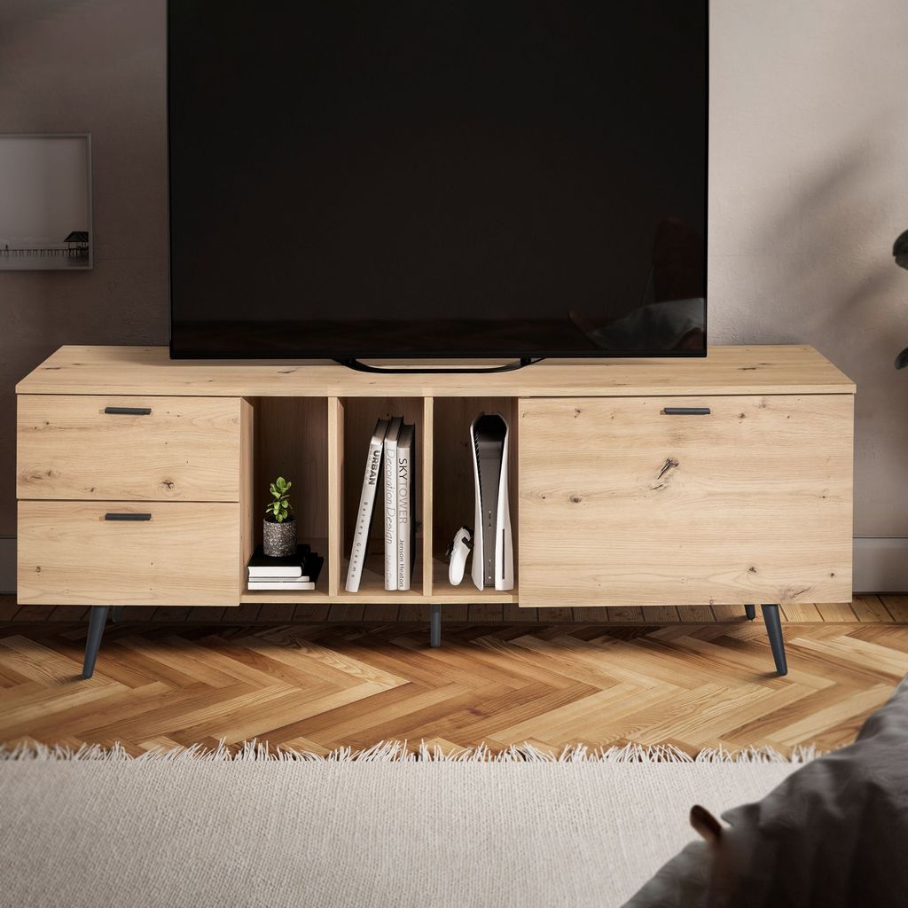 A modern wooden TV stand with drawers and shelves, holding books and a game console, in a living room setting.