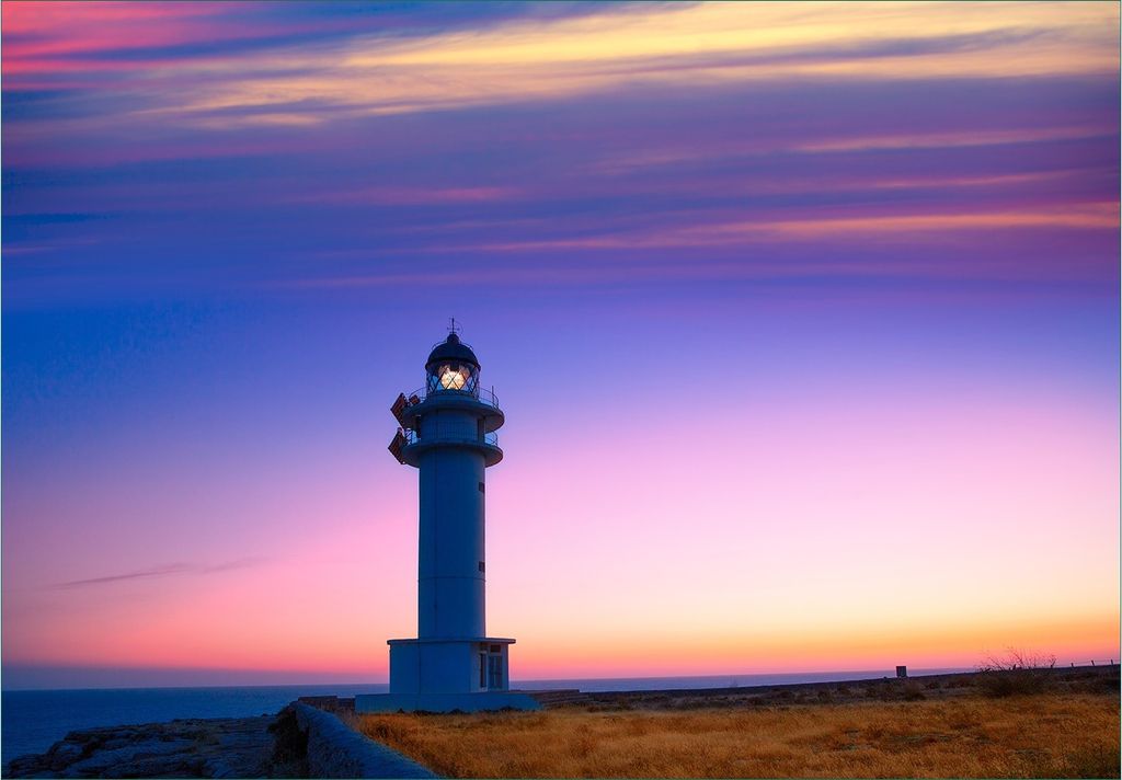 Wallario Fototapete Vliestapete, seidenmatte Oberfläche, einfache Verarbeitung, Größe 350 x 245 cm, Motiv Leuchtturm am Abend auf den Balearen M...