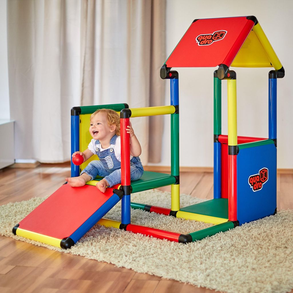 A baby is playing on a colorful modular playhouse structure indoors.
