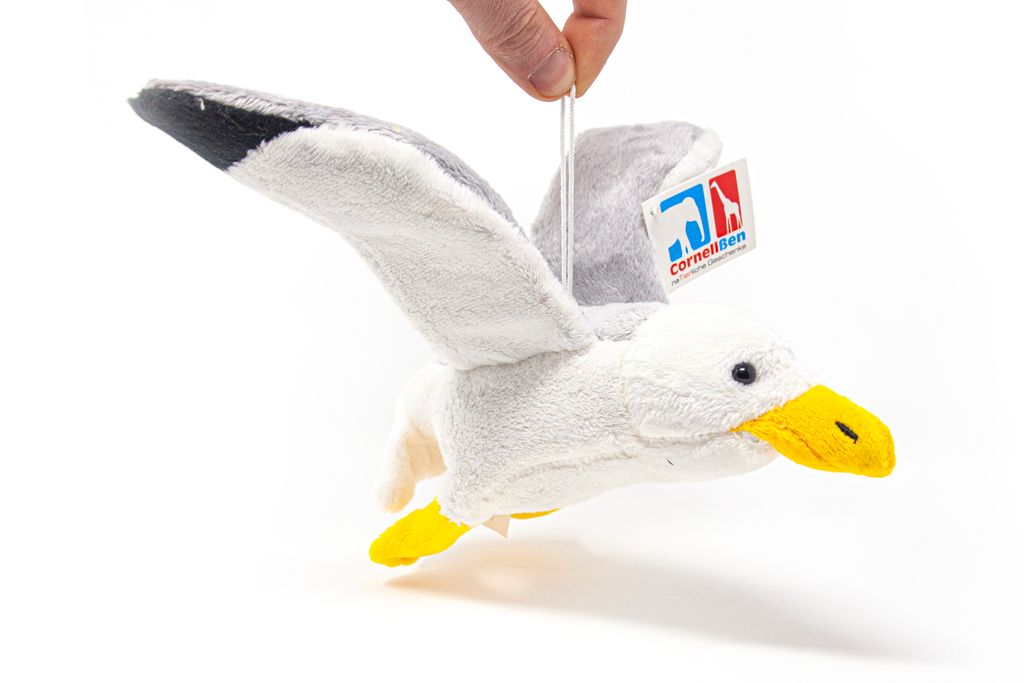 A hand holding a plush seagull toy by a string.