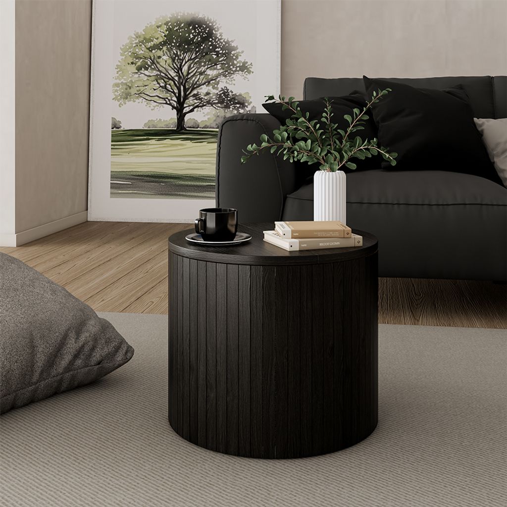 A dark wooden round coffee table with books and a cup on it, placed next to a sofa and a large framed picture of a tree.