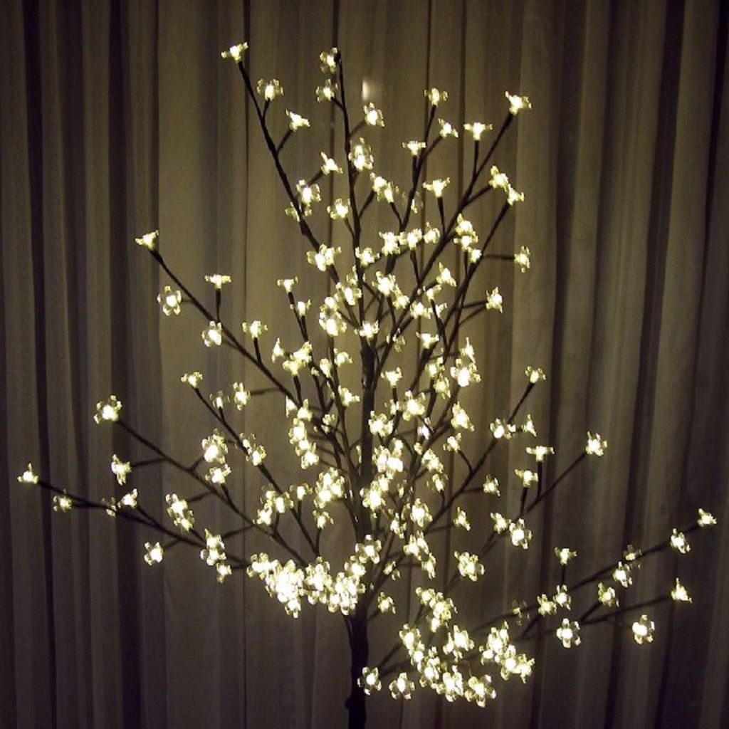 A decorative LED tree with warm white lights against a curtain background.