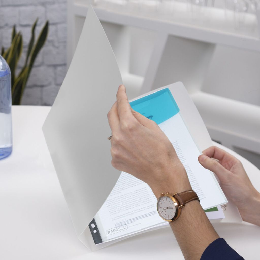 A person is holding and looking at documents in a clear plastic folder on a white table.