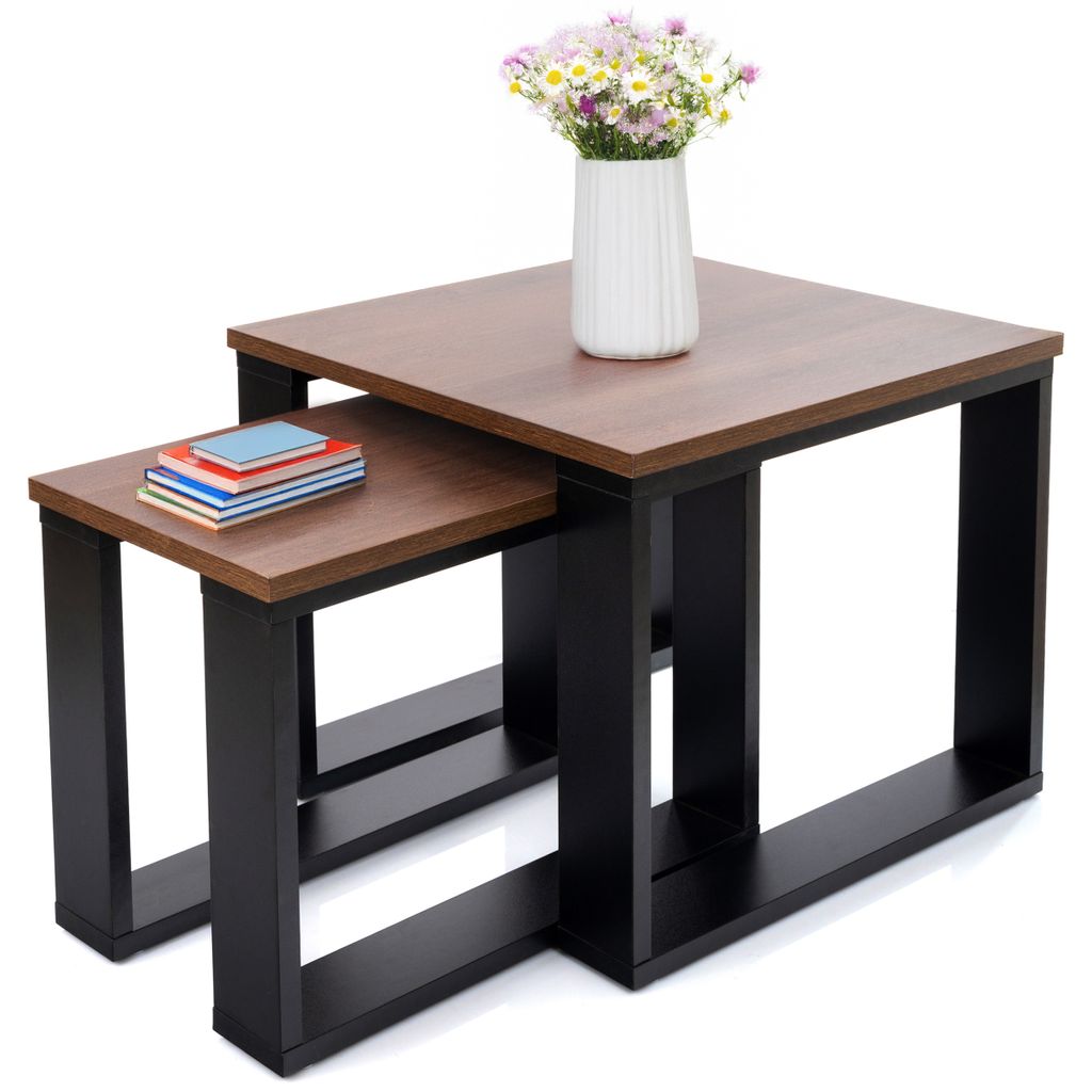 Two nesting coffee tables with wooden tops and black frames, one small stack of books on the smaller table, and a vase of flowers on the larger table.