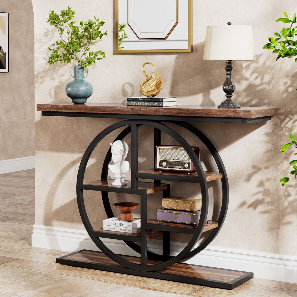 A console table with a circular shelf unit is placed against a textured wall, decorated with a vase of greenery, a gold swan sculpture, books, a vintage radio, and decorative boxes.