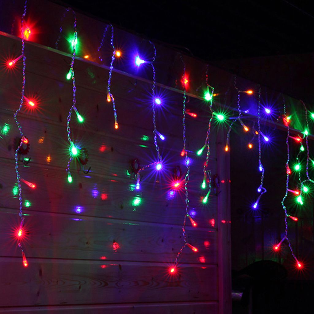 Colorful LED icicle lights hanging on a wooden wall at night.