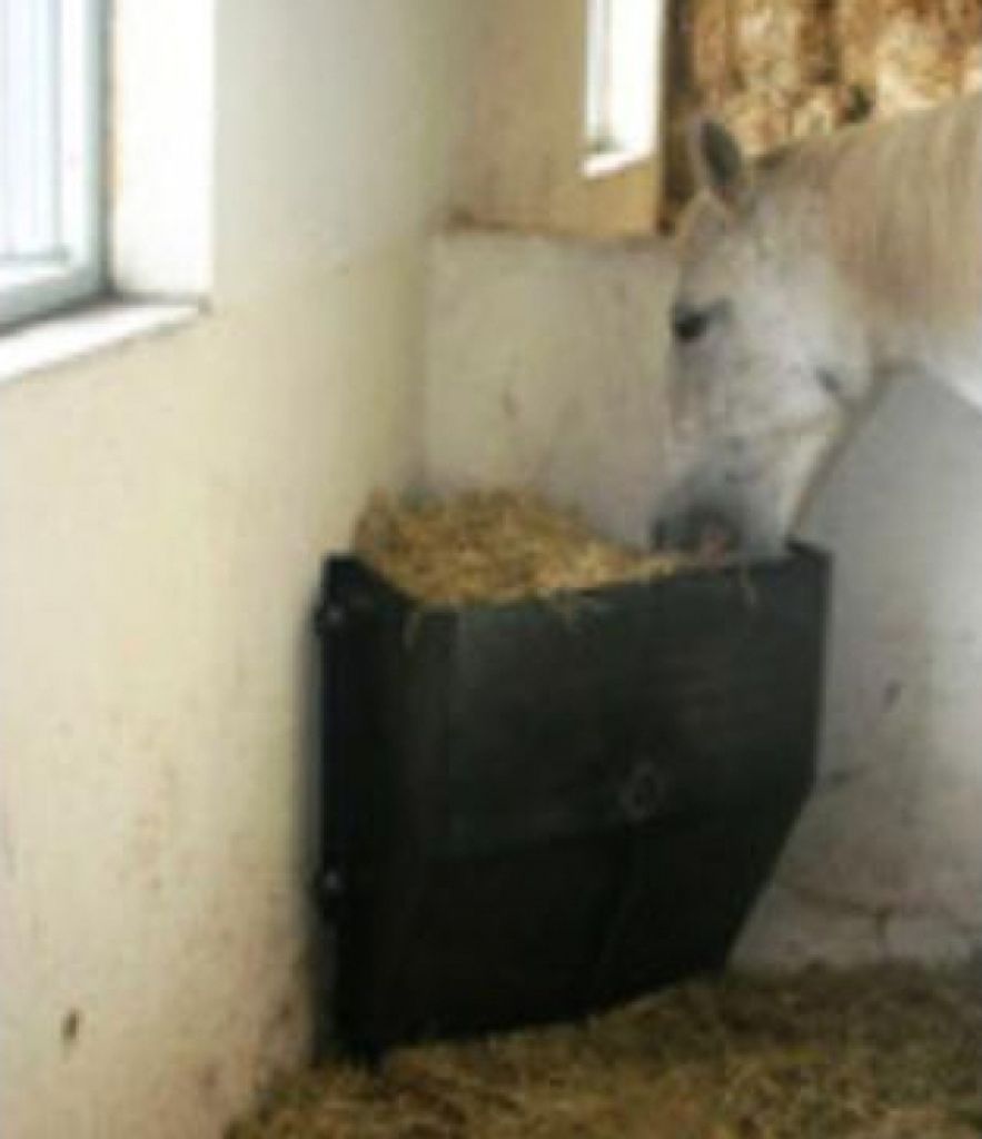 A horse eating hay from a feeder in a stable.