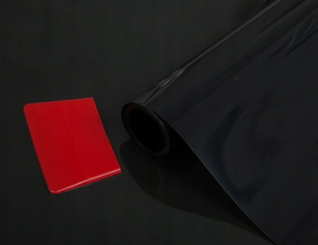 A roll of black tinting film and a red squeegee are placed on a black reflective surface.