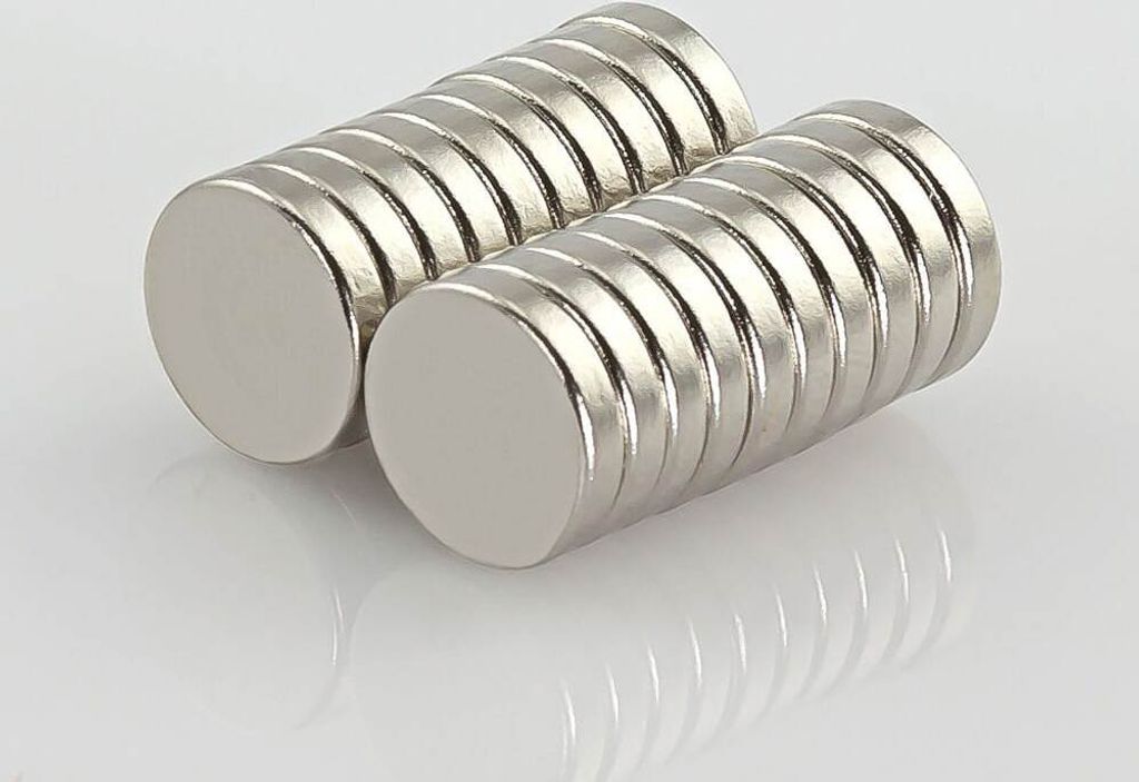 Two stacks of round, silver-colored magnets are shown on a reflective surface.