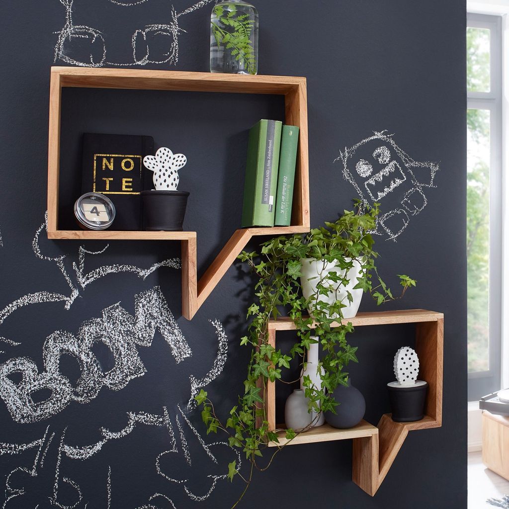 Two wooden shelves shaped like speech bubbles are mounted on a dark wall with chalk drawings. One shelf holds books and decorative items, while the other has plants and vases.