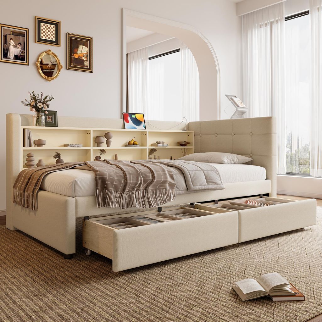 A beige daybed with storage drawers and a bookshelf headboard is shown in a well-lit room with sheer curtains and decorative items on the shelves.